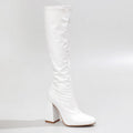 The La Gogo Calf Boot in White Wet Look showcases a chic knee-high silhouette with a chunky block heel. Crafted from vegan patent material, it features a smooth, shiny finish with a rounded toe, exuding minimalist elegance against a light gray background.